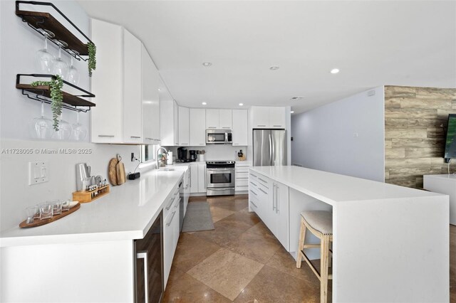 kitchen featuring a center island, a breakfast bar, appliances with stainless steel finishes, white cabinets, and beverage cooler