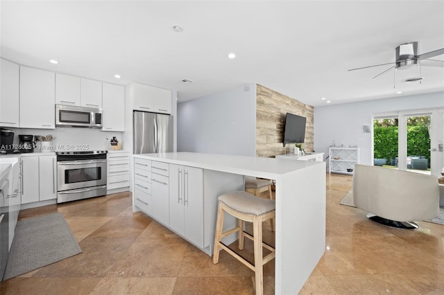 kitchen with ceiling fan, a kitchen island, a breakfast bar area, stainless steel appliances, and white cabinets