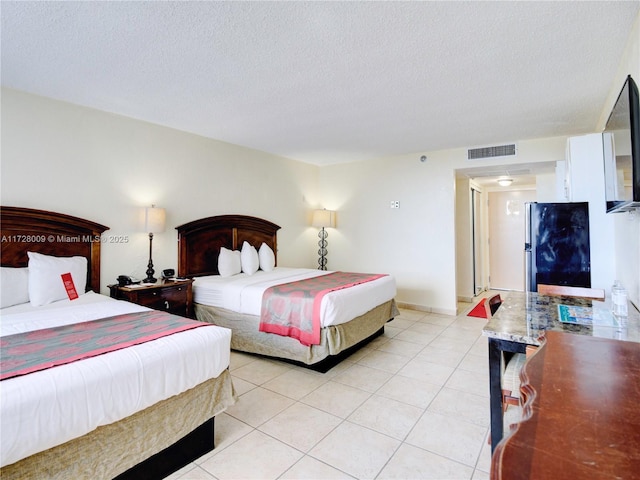 bedroom with light tile patterned floors, stainless steel fridge, and a textured ceiling