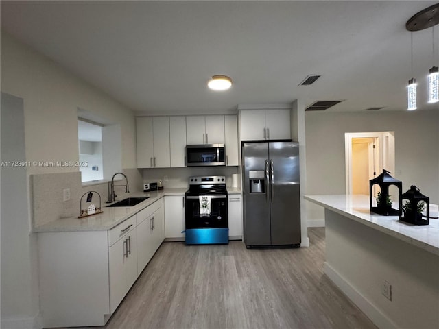 kitchen featuring sink, white cabinetry, light hardwood / wood-style flooring, hanging light fixtures, and appliances with stainless steel finishes