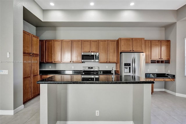 kitchen with appliances with stainless steel finishes, a center island with sink, and dark stone countertops