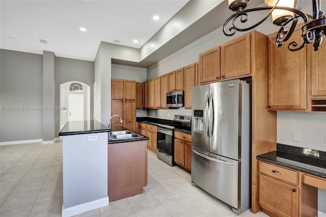 kitchen with dark stone countertops, sink, light tile patterned flooring, an island with sink, and stainless steel appliances