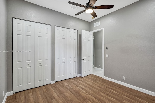 unfurnished bedroom with ceiling fan, hardwood / wood-style flooring, and multiple closets