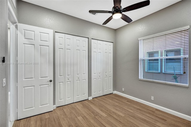 unfurnished bedroom featuring ceiling fan, two closets, and light hardwood / wood-style flooring