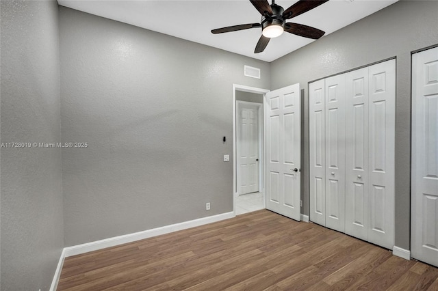 unfurnished bedroom with ceiling fan, light wood-type flooring, and two closets