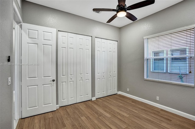 unfurnished bedroom featuring ceiling fan, two closets, and light wood-type flooring