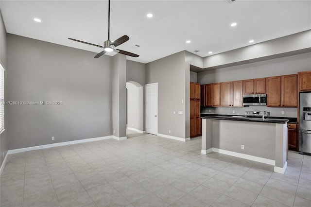 kitchen with appliances with stainless steel finishes, a towering ceiling, a kitchen island, ceiling fan, and light tile patterned floors