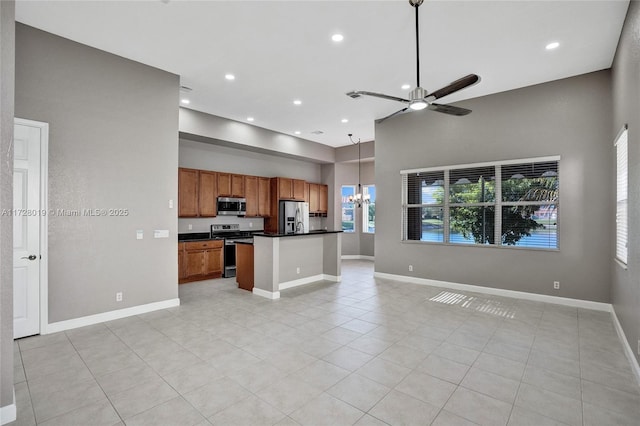 kitchen featuring a center island, a towering ceiling, hanging light fixtures, stainless steel appliances, and ceiling fan with notable chandelier