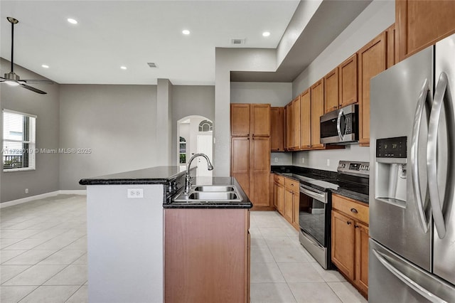 kitchen featuring stainless steel appliances, sink, ceiling fan, light tile patterned floors, and a center island with sink