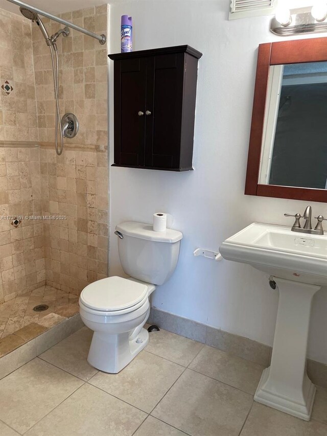 bathroom featuring sink, tile patterned floors, a tile shower, and toilet