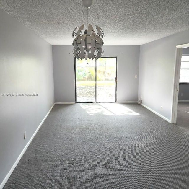 carpeted empty room featuring plenty of natural light, a textured ceiling, and a notable chandelier