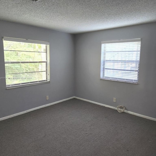 spare room with dark carpet, a textured ceiling, and a healthy amount of sunlight