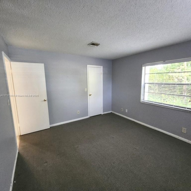 spare room featuring a textured ceiling and dark colored carpet