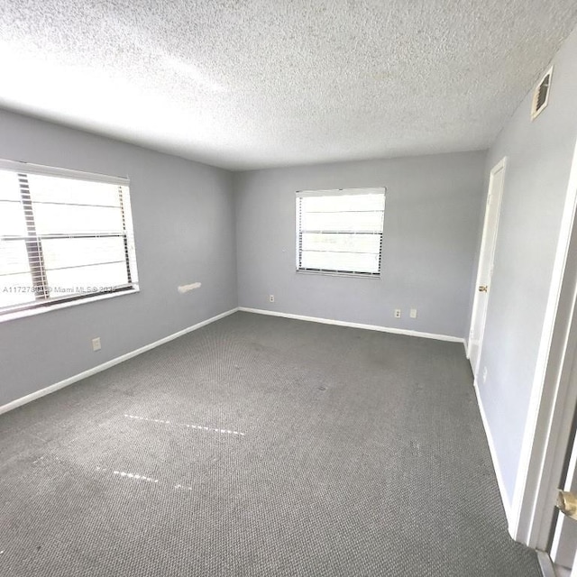 empty room with a textured ceiling and dark colored carpet