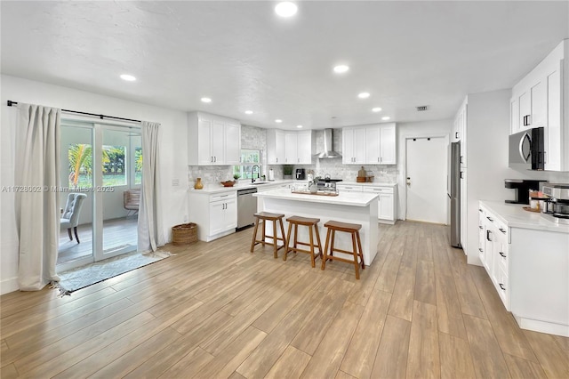 kitchen with a center island, white cabinetry, wall chimney range hood, stainless steel appliances, and a breakfast bar area