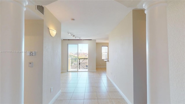 hall with decorative columns, rail lighting, and light tile patterned flooring