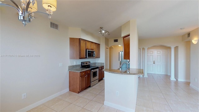 kitchen with appliances with stainless steel finishes, ornate columns, sink, light stone counters, and light tile patterned floors