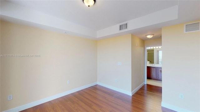 empty room with wood-type flooring and a raised ceiling