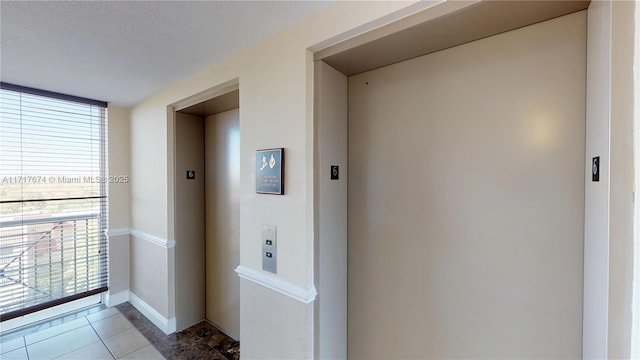 interior space with a textured ceiling, light tile patterned floors, and elevator