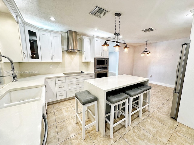 kitchen featuring a breakfast bar, white cabinetry, hanging light fixtures, stainless steel appliances, and wall chimney exhaust hood