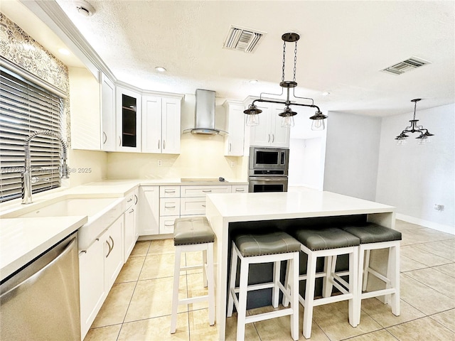 kitchen with white cabinets, a center island, wall chimney range hood, stainless steel appliances, and a notable chandelier