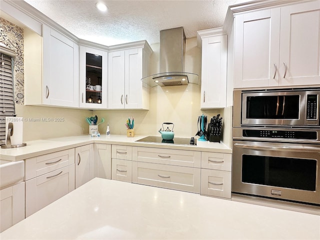 kitchen featuring stainless steel microwave, wall chimney range hood, a textured ceiling, white cabinets, and black electric cooktop