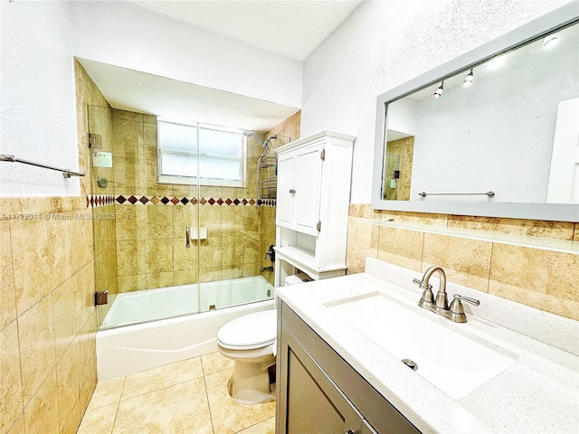 full bathroom with toilet, bath / shower combo with glass door, tile walls, and vanity