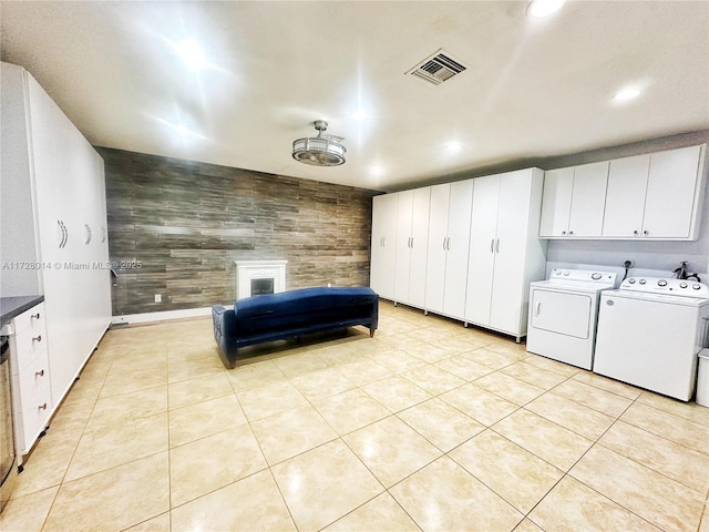 washroom featuring washing machine and dryer, cabinets, light tile patterned floors, and wood walls