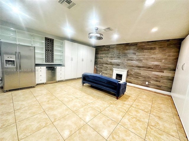 interior space featuring wine cooler, stainless steel refrigerator with ice dispenser, light tile patterned flooring, and wood walls