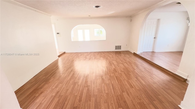 spare room with light hardwood / wood-style floors, a textured ceiling, and crown molding