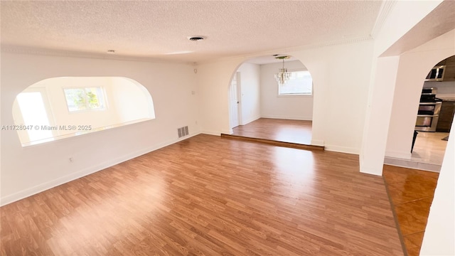 empty room with a notable chandelier, ornamental molding, a textured ceiling, and hardwood / wood-style floors