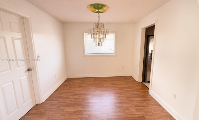 unfurnished dining area with light wood-type flooring, a notable chandelier, and a textured ceiling