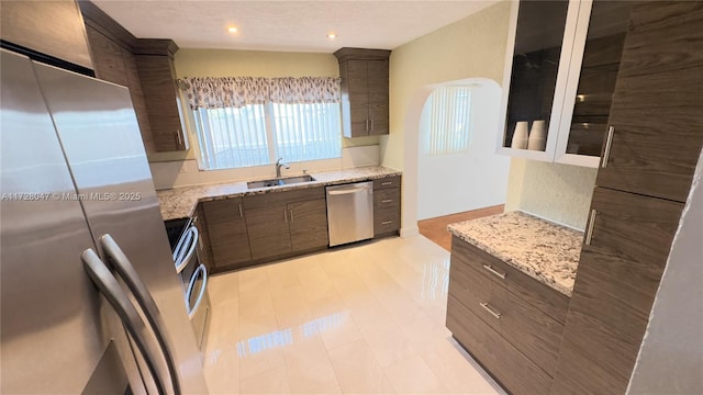 kitchen featuring light stone countertops, sink, appliances with stainless steel finishes, and dark brown cabinets