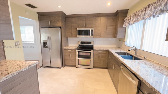 kitchen with light stone countertops, sink, appliances with stainless steel finishes, and light tile patterned floors