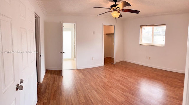 unfurnished bedroom with ceiling fan, a closet, ornamental molding, a walk in closet, and light hardwood / wood-style flooring