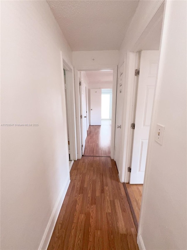 corridor with a textured ceiling and dark wood-type flooring