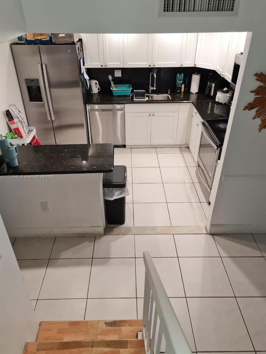 kitchen featuring white cabinets, backsplash, light tile patterned floors, and stainless steel appliances