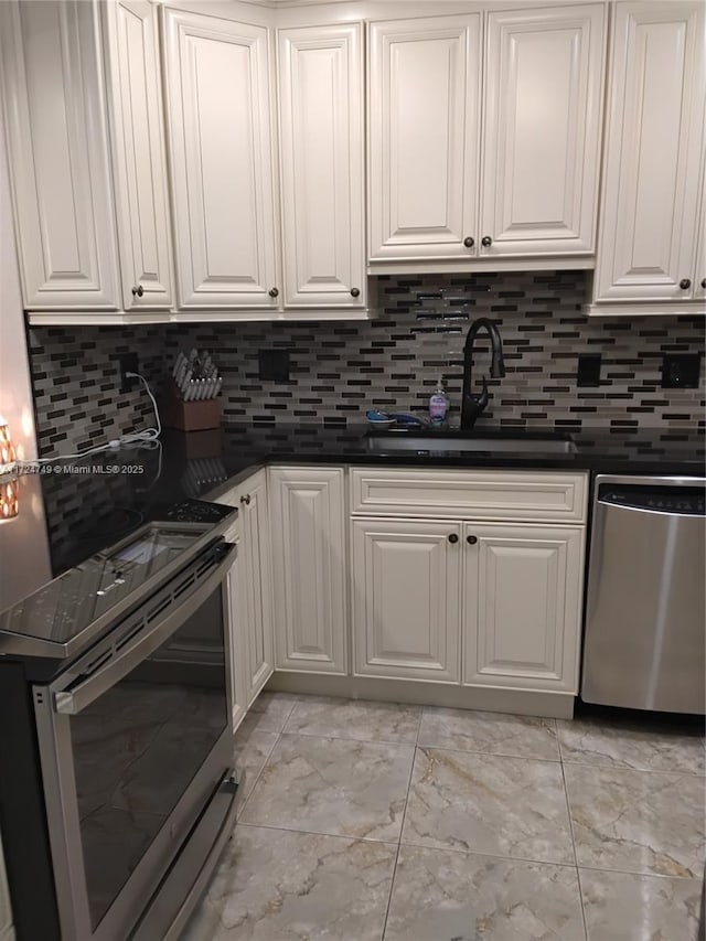 kitchen with stainless steel appliances, dark countertops, tasteful backsplash, white cabinets, and a sink