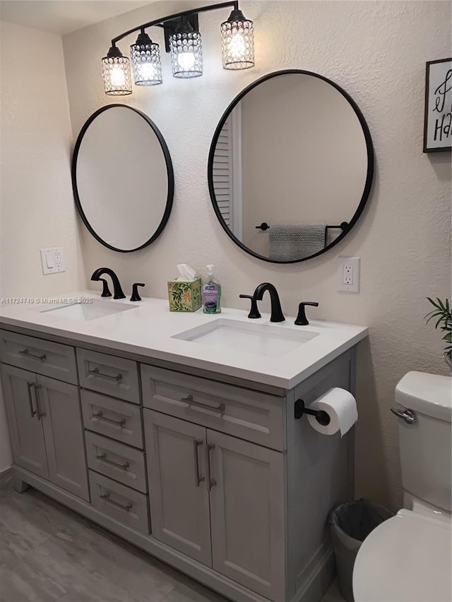 bathroom featuring a textured wall, a sink, toilet, and double vanity