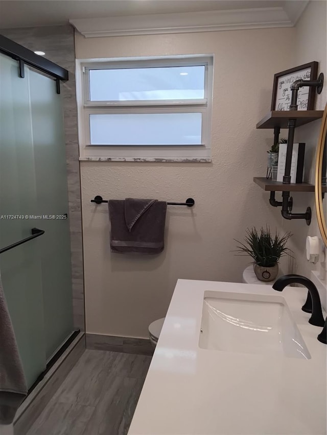 bathroom featuring crown molding, toilet, a sink, a shower stall, and wood finished floors