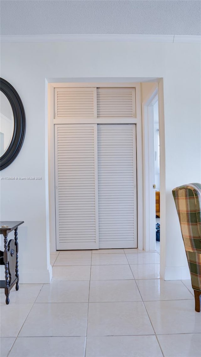 hallway featuring a textured ceiling, light tile patterned flooring, and ornamental molding