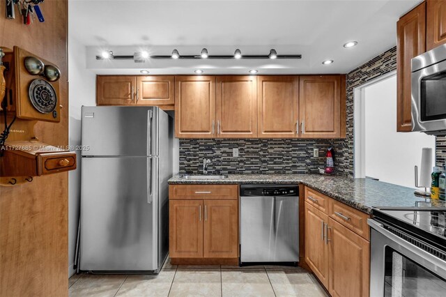 kitchen with light tile patterned flooring, sink, decorative backsplash, dark stone counters, and stainless steel appliances