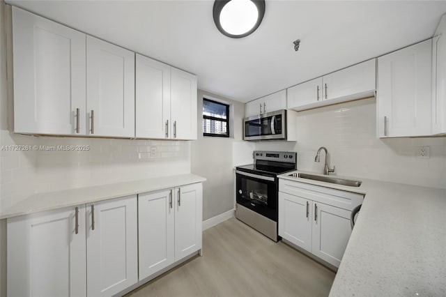 kitchen with white cabinets, sink, stainless steel appliances, and light hardwood / wood-style flooring