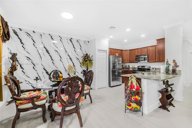 kitchen with light stone countertops, appliances with stainless steel finishes, a kitchen breakfast bar, ornamental molding, and kitchen peninsula