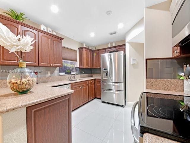 kitchen with light stone countertops, appliances with stainless steel finishes, sink, backsplash, and light tile patterned floors