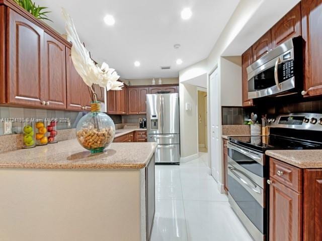 kitchen with pendant lighting, decorative backsplash, appliances with stainless steel finishes, light tile patterned floors, and light stone counters