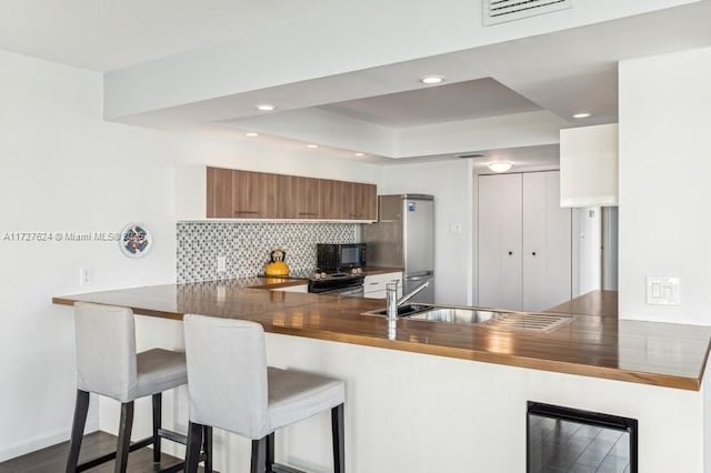 kitchen featuring dark hardwood / wood-style floors, a breakfast bar area, kitchen peninsula, and stainless steel fridge