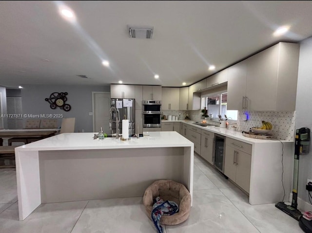 kitchen featuring stainless steel appliances, a kitchen island, beverage cooler, and decorative backsplash