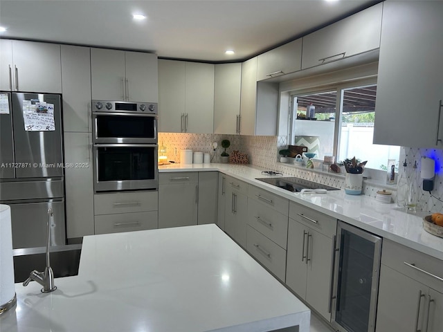 kitchen with light stone countertops, beverage cooler, appliances with stainless steel finishes, backsplash, and gray cabinets