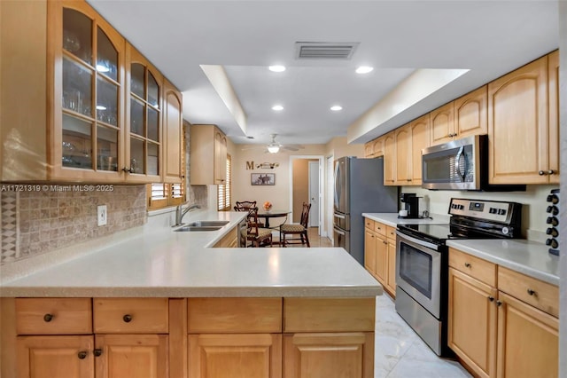 kitchen with ceiling fan, kitchen peninsula, sink, a tray ceiling, and stainless steel appliances